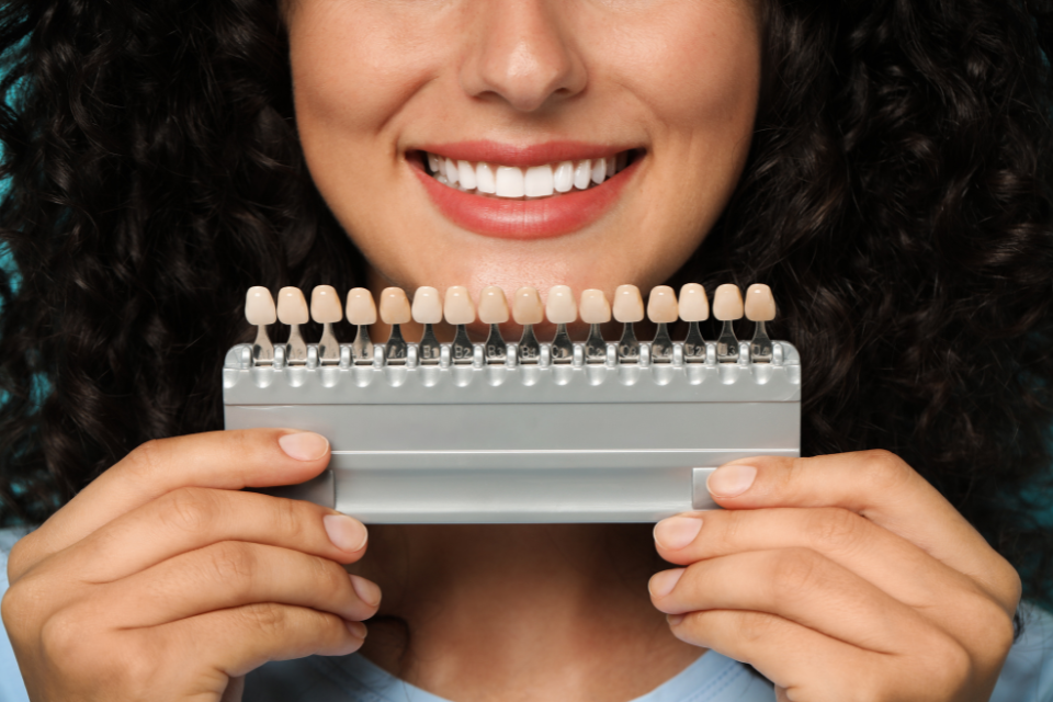 Patient holding a dental shade guide to match custom porcelain veneers for a smile redesign in Shelton.